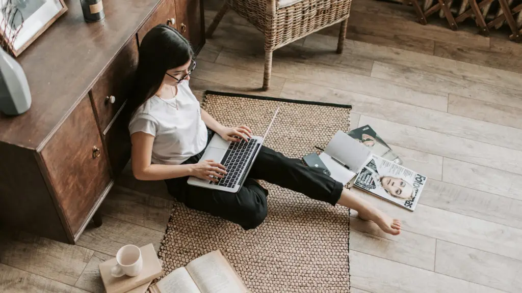 confident-young-businesswoman-with-laptop-and-notebook-sitting-on-floor-modern-apartment