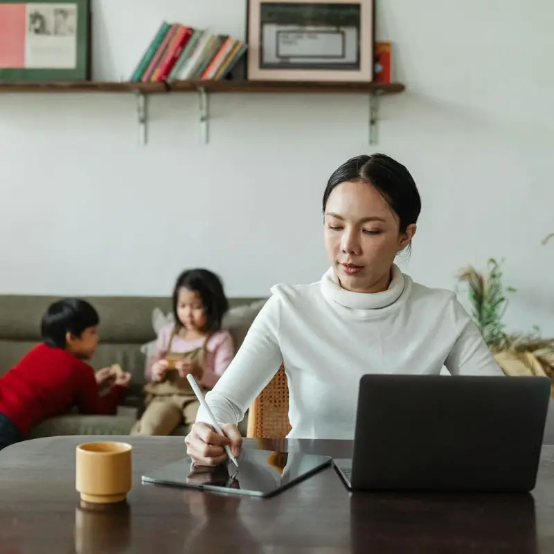 focused-young-asian-mother-working-remotely-while-children-playing-on-sofa